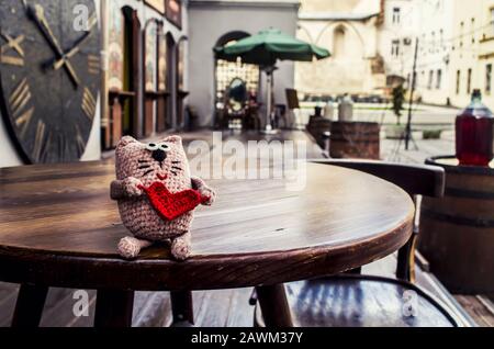 Adorable chat crocheté avec coeur rouge sur fond de vieille ville.concept de Saint-Valentin. Banque D'Images