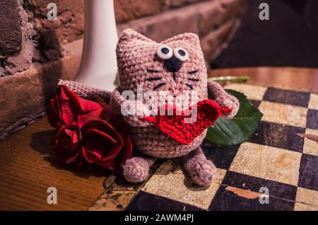 Adorable chat crochetté au cœur rouge avec rose rouge sur fond vintage d'échecs. .concept de Saint-Valentin. Banque D'Images