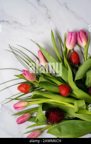 Gros plan d'un beau bouquet de fleurs avec fraises rouges sur une table en marbre avec espace pour le texte. Printemps, été, tulipes Banque D'Images