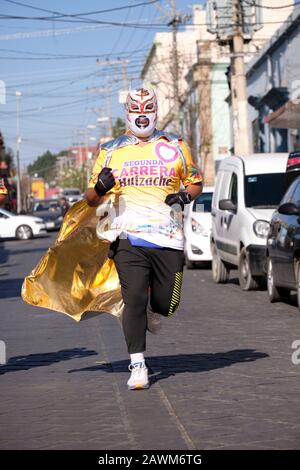 Oaxaca De Juarez, Mexique. 9 février 2020. Un homme vêtu d'un costume Lucha libre finissant sa course de 10 km, l'un des coureurs de la deuxième course annuelle Huizache Athletic Race à travers les rues de la vieille partie coloniale de la capitale. Banque D'Images