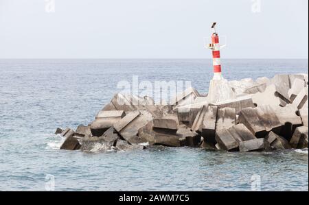 Tour à éclats rayés rouge et blanc debout sur le brise-lames d'entrée de Marina da Calheta. Madère, Portugal Banque D'Images