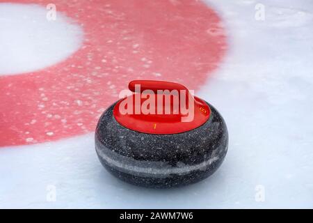 Une pierre de curling rouge sur la glace près d'un centre d'une maison Banque D'Images