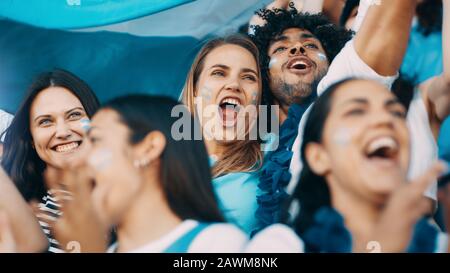 Les fans de sport excités lors des matchs en direct criant et applaudissant pour leur équipe. Les gens qui regardent un match de football chantent pour encourager l'équipe nationale argentine. Banque D'Images