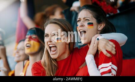 Des spectateurs féminins applaudissaient à un événement sportif. Les supporters de l'équipe de football allemande applaudissant et chantent activement dans la foule. Banque D'Images