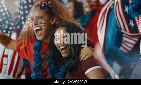 Fans enthousiastes avec le drapeau américain dans la foule sportive célébrant le succès de l'équipe. Un groupe de fans de football américains se réjouient dans des stands. Banque D'Images