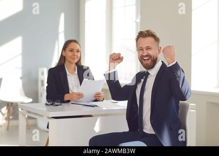 Entretien réussi. Un homme en costume se réjouit d'un nouvel emploi assis à une table avec une femme employeur dans un bureau blanc. Banque D'Images