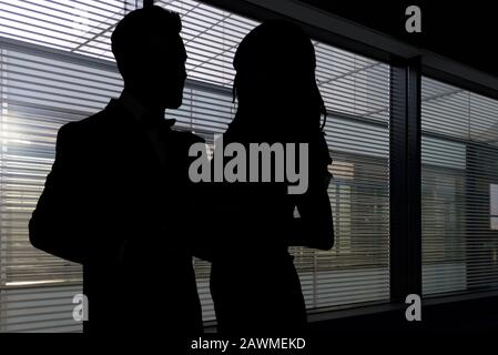 Image conceptuelle du romantisme au travail - silhouettes d'une femme et d'un homme s'embrassant dans un sombre bureau d'entreprise Banque D'Images