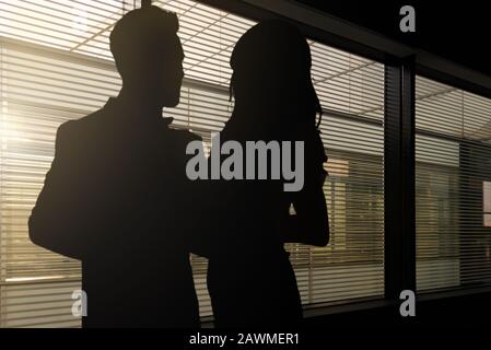 Image conceptuelle du romantisme au travail - silhouettes d'une femme et d'un homme s'embrassant dans un sombre bureau d'entreprise Banque D'Images