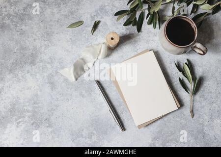 Moody féminin mariage papeterie scène maquette. Carte de vœux vierge, tasse de café, stylo argenté avec feuilles d'olive, branches. Fond de la table Grunge Banque D'Images