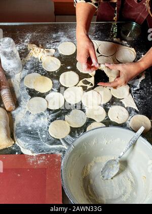 Une femme qui utilise un rouleau et un verre prépare des blancs de pâte ronde pour modéliser des boulettes dans la cuisine nationale ukrainienne. Banque D'Images