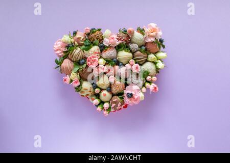 Boîte en forme de coeur avec fraises enrobées de chocolat fait à la main avec différents garnitures et fleurs comme présents sur la Saint Valentin sur fond mauve Banque D'Images