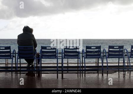 Homme assis sur une chaise qui regarde l'océan sous un ciel nuageux Banque D'Images
