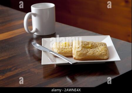 Tasse à café à côté de la plaque carrée avec deux miettes et un couteau en acier inoxydable placé sur le coin d'une table en bois Banque D'Images