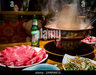 Hotpot mongol avec tranches de viande servies à la table du restaurant avec bière locale Tsingtao, quartier Xi Cheng Hutong, Pékin, Chine, Asie Banque D'Images