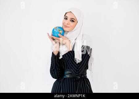 Jolie jeune femme dans le hijab embrassant un petit globe terrestre. Entretien de la planète, sauver la terre, écologie, concept de voyage. Banque D'Images