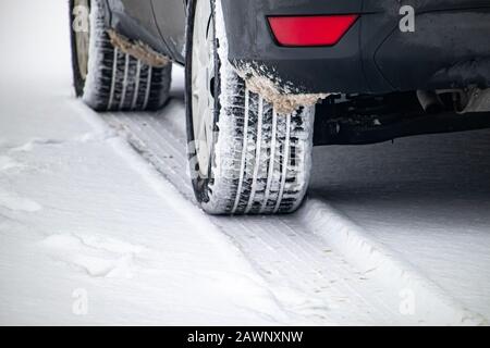 Les pneus d'une automobile sont enfilés dans la neige lorsque le véhicule est arrêté dans un parking. La neige fraîche a laissé de la neige enchâssée dans les bandes de roulement. Banque D'Images