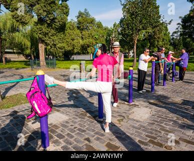 Les personnes plus âgées chinoises qui font de l'exercice dans une salle de sport en plein air avec une femme qui s'étire sur la jambe, Tiantan Park, Beijing, Chine Banque D'Images