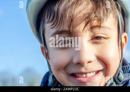 Portrait d'un jeune garçon à l'extérieur portant un casque de vélo et souriant. Banque D'Images