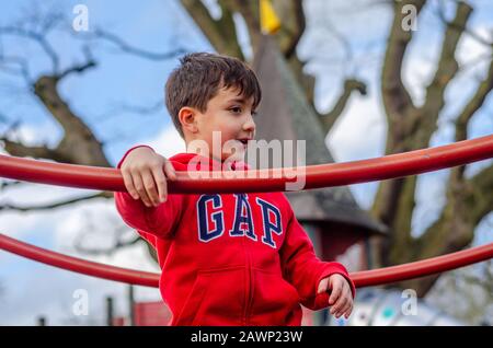 Un jeune garçon heureux de jouer sur un cadre d'escalade dans une aire de jeux pour enfants. Banque D'Images