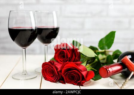 Concept Saint Valentin. Deux verres de vin, bouteille de vin, tire-bouchon et roses rouges sur une table en bois blanc. Mise au point sélective. Banque D'Images