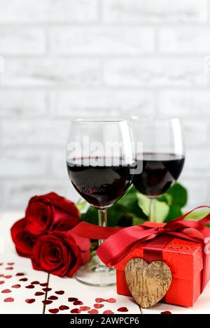 Concept Saint Valentin. Deux verres de vin, roses rouges, boîte à cadeaux et coeur en bois sur une table en bois blanc. Mise au point sélective. Banque D'Images