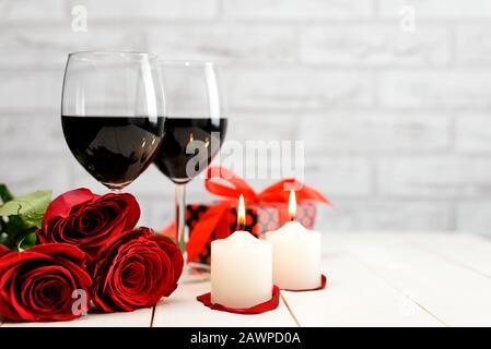 Concept Saint Valentin. Deux verres de vin, roses rouges, boîte cadeau et bougies brûlantes sur une table en bois blanc avec espace pour le texte. Fcu sélectif Banque D'Images