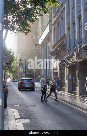 En regardant La Petite rue Bourke vers la rue Queen, en fin d'après-midi, le soleil s'écoule vers le bas et deux femmes traversent après un passage de voiture. Banque D'Images