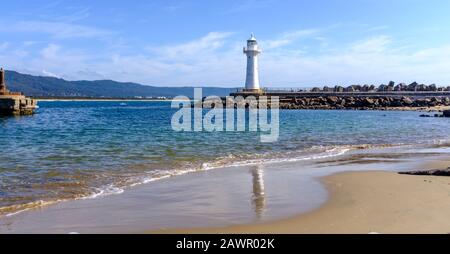 Vue sur la plage du bassin de Belmore jusqu'au vieux phare du port de Wollongong situé au bout du brise-lames à l'entrée du port. Banque D'Images