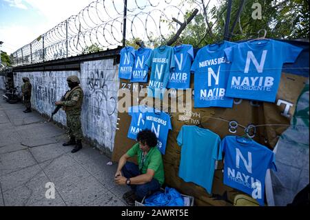 San Salvador, El Salvador. 9 février 2020. Un soldat se tient devant le congrès comme un homme vend des t-shirts du président salvadorien Nayib Bukele. Le président salvadorien Nayib Bukele a été élu au Congrès accompagné de dizaines de soldats et menacé par les législateurs d'approuver un prêt pour un plan de sécurité après avoir appelé à une session de congrès d'urgence.Bukele a tenu un rassemblement à l'extérieur du Congrès salvadorien, où une foule a chanté des slogans et des menaces contre les législateurs. Crédit: Camilo Freedman/Zuma Wire/Alay Live News Banque D'Images