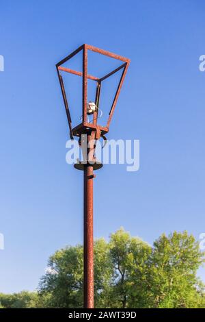 Ancienne lampe de rue rouillée avec ampoule cassée et fils électriques déchirés contre le ciel bleu d'été lumineux et les arbres verts. Dévastation et abandon de villa Banque D'Images