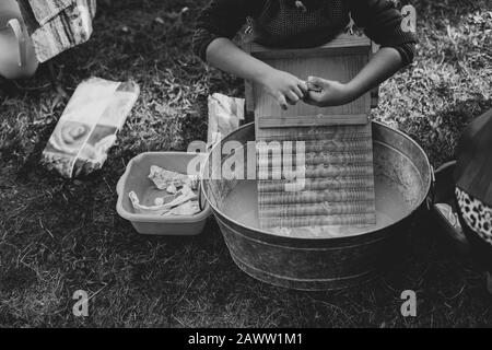 Un enfant se lave des vêtements dans une ancienne baignoire de lavage en zinc avec une planche à laver en bois Banque D'Images