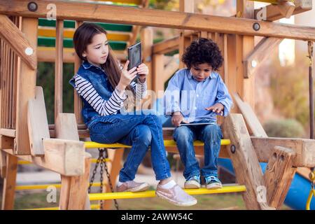 Deux enfants garçon et fille jouant à des jeux sur tablette en plein air. Concept de dépendance des enfants et des gadgets Banque D'Images