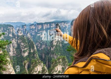 Une jeune fille touristique asiatique prend une photo à l'aide d'un smartphone au parc forestier national de Zhangjiajie, site classé au patrimoine mondial de l'UNESCO, Wulingyuan, Hunan, Chine Banque D'Images