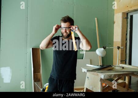 Heureux homme barbu debout avec un dirigeant d'angle dans l'appartement rennovant. Banque D'Images