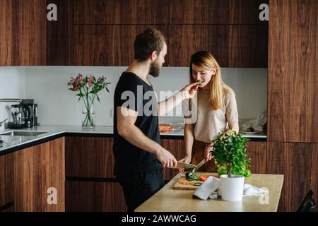 Femme coupe des légumes, tandis que son petit ami nourrissant ses tranches de concombre Banque D'Images