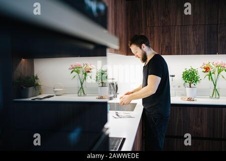 Homme barbu d'âge moyen laver la vaisselle et les ustensiles à l'évier de cuisine Banque D'Images