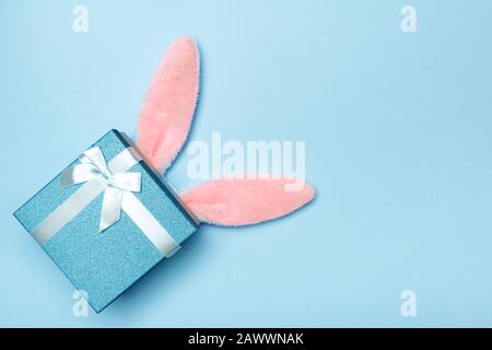 Easter lapin doux oreilles avec une boîte cadeau sur un fond bleu. Espace de copie vue du dessus plat. Banque D'Images