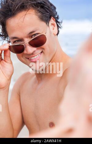 Bel homme d'Asie biracial sur la plage de vacances portant des lunettes de soleil souriant Banque D'Images