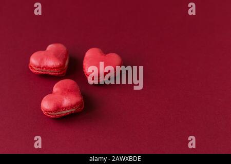 Macarons en forme de coeur sur un fond rouge foncé. Concept pour la Saint Valentin. Placer pour le texte. Banque D'Images