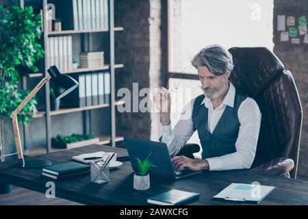 Concentré ancien directeur immobilier barbu propriétaire société assis table bureau utiliser ordinateur portable lire son rapport de col analyser regarder écran lunettes de maintien Banque D'Images