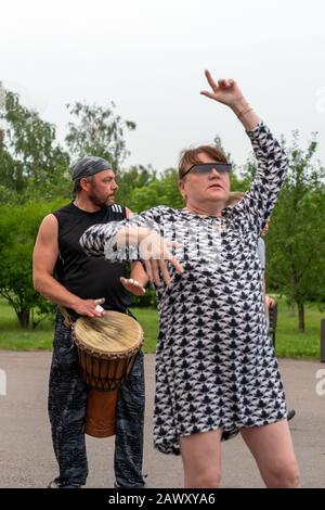 Krasnoyarsk, Russie, 30 juin 2019: Une femelle adulte dans des danses de lunettes à la batterie africaine Tam Tam djembe dans un parc public. Fête, photo verticale. Banque D'Images