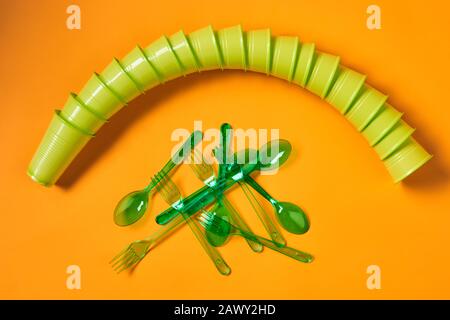 Plan horizontal plat de jeu de tasses en plastique vert jetables, cuillères et fourchettes sur fond orange vif Banque D'Images