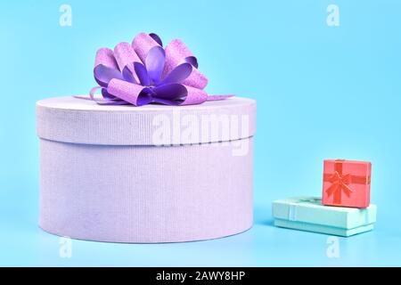 Boîte cadeau ronde avec noeud et deux petites boîtes cadeaux. Boîte violette fermée pour cadeau sur fond bleu. Forfaits surprise pour les vacances: Anniversaire, Vale Banque D'Images