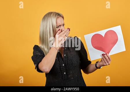 fille choquée nerveux irritée femme mise la main sur la bouche semble papier coeur rouge Banque D'Images