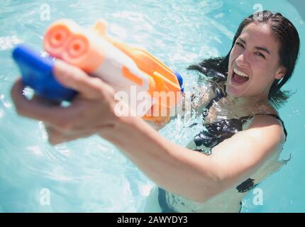 Portrait femme ludique avec pistolet dans la piscine ensoleillée Banque D'Images