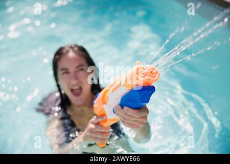 Une femme espiègle à l'aide d'un pistolet dans la piscine d'été ensoleillée Banque D'Images