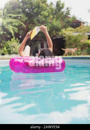 Femme relaxant, livre de lecture sur radeau gonflable dans la piscine d'été ensoleillée Banque D'Images
