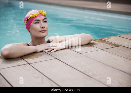 Femme confiante dans la casquette de natation et les lunettes de protection penchant sur le bord de la piscine Banque D'Images