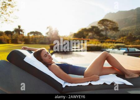 Une jeune femme sereine dans un maillot de bain relaxant, bronzer sur un patio de luxe Banque D'Images