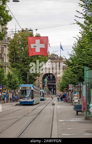 Promenade commerçante appelée Bahnhofstrasse, centre-ville de Zurich. Tram / train avec drapeau suisse en face. Banque D'Images